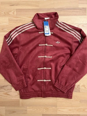 Adidas Originals CNY Chinese New Year Tang Jacka S röd NY - Den virala Adidasjackan säljes, köptes i Kina där denna kollektion säljs exklusivt, mycket sällsynt och svår att få tag på. Helt ny och oanvänd, 100% äkta prislappen är kvar. Stor i storleken. Oversized look.