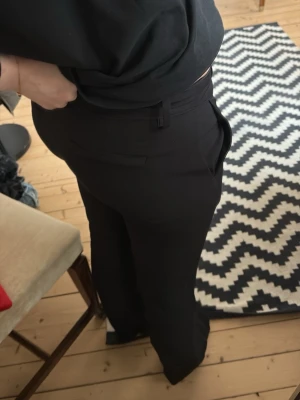 Svarta kostymbyxor med bootcut - Säljer ett par svarta kostymbyxor med bootcut passform och hög midja. Byxorna har bälteshällor och klassisk design utan synliga detaljer. Perfekta till en snygg outfit när du vill känna dig extra stilsäker.