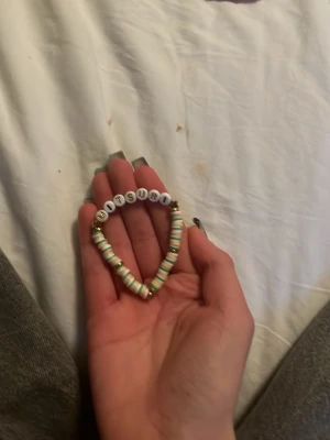 Färgglatt pärlarmband med text - Ett handgjort armband med färgglada platta pärlor i pastellfärger och vita bokstavspärlor som stavar 'MITSURI'. Armbandet har även små guldfärgade detaljer och elastisk tråd för enkel användning. Perfekt accessoar för dig som gillar personliga smycken.