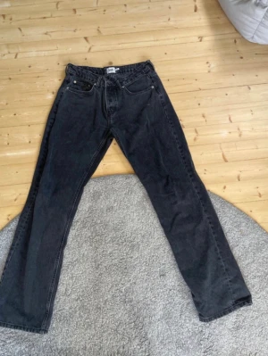 Svarta Icon jeans  - Klassiska svarta Levi's 501 jeans med rak passform och knappgylf. Jeansen har fem fickor och är tillverkade i slitstark bomullsdenim. Perfekta för dig som gillar en tidlös och avslappnad stil.