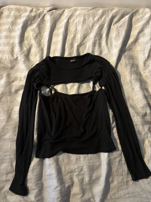 Svart långärmad med inbyggt linne - Trendig svart långärmad topp från Gina Tricot med croppad design och cut out-detalj över bröstet. Toppen har smala axelband och en unik look som sticker ut. Perfekt för dig som vill ha något edgy och stilrent i garderoben.