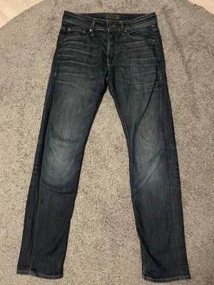 Mörkblå jeans från Jack & Jones - Snygga mörkblå jeans från Jack & Jones med klassisk femficksdesign och diskreta slitningar. Jeansen har storlek 28/32