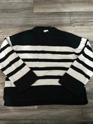 Randig stickad tröja från Gina Tricot - Säljer en svartvit stickad tröja från Gina Tricot med breda horisontella ränder. Tröjan har rund halsringning och ribbade muddar vid ärmslut och nederkant. Perfekt för dig som gillar klassisk och avslappnad stil.
