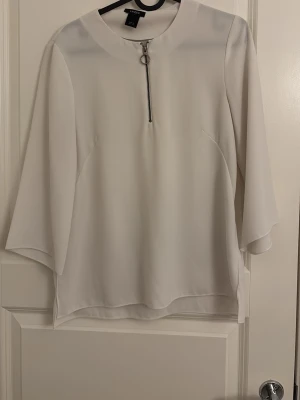 Vit blus med dragkedja från Lindex - Stilren vit blus från Vero Moda med trekvartsärm och en cool dragkedja framtill. Blusen har en rak passform och är gjord i ett lätt, mjukt tyg som ger ett snyggt fall. Perfekt att matcha med jeans eller kjol för en trendig look.