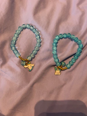 Blå pärlarmband med Sanrio-berlocker - Två söta armband med blå glaspärlor och små guldiga detaljer. Varje armband har en Sanrio-berlock, en med Cinnamoroll och en med Kuromi. Perfekt accessoar för dig som gillar kawaii-stil och vill ha något unikt och färgglatt.