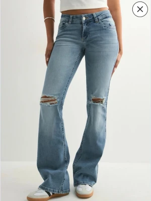 Bootcut ljusblå jeans med slitningar - Säljer ett par ljusblå bootcut jeans med slitningar över knäna och snygga detaljer på bakfickorna. Jeansen har hög midja och är tillverkade i klassiskt denimtyg. Perfekta för en avslappnad och trendig look. Original pris: 699, dom är aldrig använda så helt nya. 