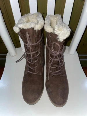 Bruna stövletter med snörning - Snygga bruna stövletter i mocka med kilklack och snörning framtill. Fodrade med fuskpäls. Klackhöjd 7 cm. 