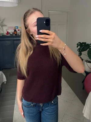 Vinröd stickad tröja med halvärm - Mysig vinröd stickad tröja med halvärm och högre rund halsringning. Tröjan har en rak passform och är perfekt att styla med jeans. Materialet ser ut att vara mjukt och bekvämt, troligen bomull eller ullblandning.