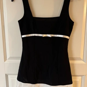 Svart och vit kortklänning med rosett - Supersöt kortklänning i svart med breda axelband och en vit satinrosett , storlek s