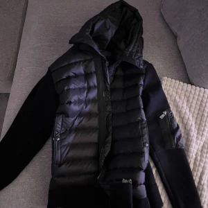 Svart Moncler med luva - Säljer en svart pufferjacka från Moncler med stickade ärmar och quiltad front. Pris kan sänkas vid snabbaffär.                                                             Storlek M men passar som S