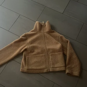 Hm Beige teddyjacka - Mysig beige teddyjacka med hög krage och två stora fickor framtill. Jackan har en hel dragkedja och är tillverkad i mjukt fleece-material som håller dig varm. Perfekt för kyliga dagar och enkel att matcha med jeans eller mjukisbyxor. Ej använd så mycket bra skick!