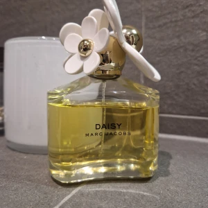 Marc Jacobs parfym  - Ikonisk parfym från Marc Jacobs med lekfull blomdetalj på korken. Flaskan innehåller 100 ml och är tillverkad i Frankrike. Perfekt för dig som vill ha en stilren och trendig doft på hyllan.