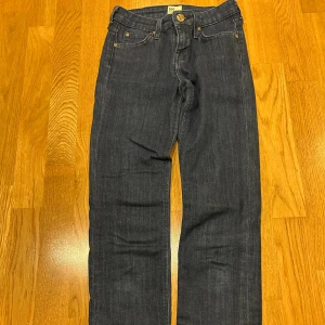 Mörkblå raka jeans från Lee - Snygga mörkblå jeans från Lee med klassisk femficksdesign och raka ben. Jeansen är tillverkade i en stretchig denim av 98% bomull och 2% elastan för extra komfort. Perfekta för dig som gillar en tidlös och clean look.