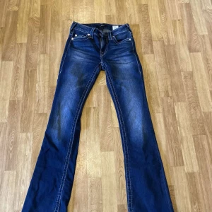 True Religion BECCA Bootcut Jeans - Snygga blå bootcut jeans från True Religion, modell BECCA Mid Rise Bootcut. Rosa sömmar på rumpan. Jeansen är i stretchig bomull och har en medellåg midja för en bekväm passform. Strlek 24 i midja. Jag är 160 och de är lite långa på mig! 