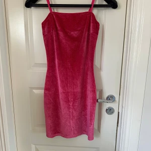 Glittrig rosa sammetsklänning - Superfin rosa sammetsklänning med glittereffekt från Femme Luxe Finery. Klänningen har tunna axelband och en kroppsnära passform som framhäver figuren. Perfekt till fest, middag eller en utekväll! Försluts med dragkedja i ryggen.  Gjort i polyester. 