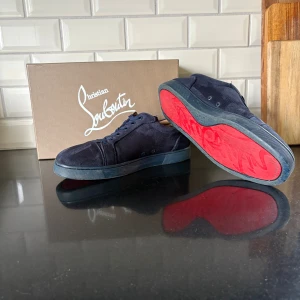Christian Louboutin mörklblåa - Snygga mörkblå sneakers från Christian Louboutin i mocka med klassisk röd sula och diskret logga på sidan. Skorna har rund tå, snörning och platt sula. Perfekta för dig som vill sticka ut med exklusiva detaljer och ikonisk design. Perfekt skick syns att de har varit använda men fortfarande extremt bra skick. Allt og tillkommer. Hör av er vid frågor kommer med snabba svar :)