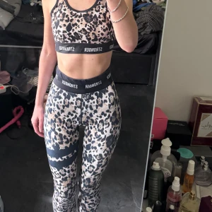 Leopardmönstrad sportset Stronger - Säljer en snygg leopardmönstrad sporttopp från Stronger med svarta och beige toner. Toppen är ärmlös med svarta elastiska band och logga runt bröstet. Perfekt för dig som vill sticka ut på gymmet!