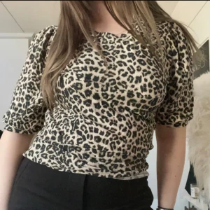 Leopardmönstrad blus - Säljer en snygg blus med leopardmönster i beige och svart. Modellen har puffiga korta ärmar och rund halsringning. Materialet är mjukt och stretchigt, perfekt för dig som vill sticka ut med ett djuriskt print. Passar dig som gillar trendiga detaljer och cool stil.