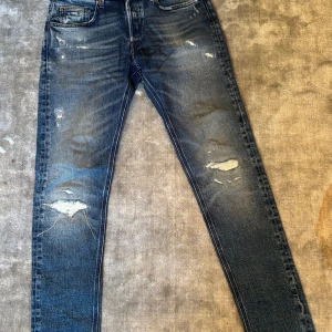 Replay jeans med slitningar - Snygga blå jeans från Replay med slitna detaljer. Storlek W29 och L32. Jeansen är i mycket bra skick och jag säljer dom eftersom dom helt enkelt aldrig kom till användning. Köpta på NK Göteborg för 2 000kr. Tillverkade i stretchig denim för en skön passform. Perfekta för dig som gillar en trendig och avslappnad look.