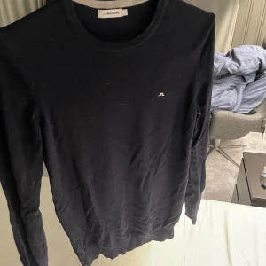 Svart tröja från J.Lindeberg - Säljer en stilren svart tröja från J.Lindeberg. Tröjan har en liten logotyp på bröstet och är tillverkad i ett mjukt material. Perfekt för en avslappnad men snygg look.