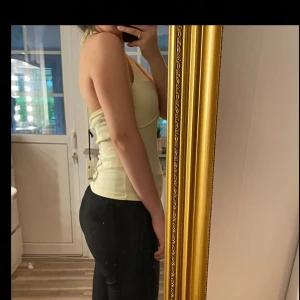 Ljusgul halterneck linnetopp - Säljer en ljusgul halterneck linnetopp med v-ringad front och smala band som knyts i nacken. Aldrig använd!