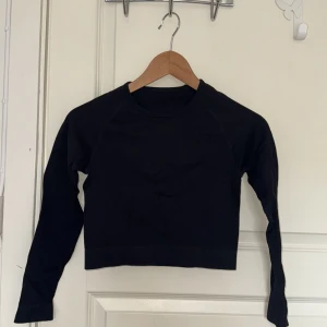 Svart ribbad croppad långärmad topp - Svart croppad topp med lång ärm och rund hals. Materialet är ribbat och stretchigt, vilket gör den bekväm och följsam. Perfekt för träning.