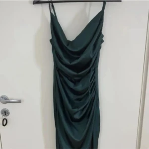 Mörkgrön långklänning med drapering - Mörkgrön lång klänning. Slits nertill. Justerbara ärmar. Dragkedja baktill. 