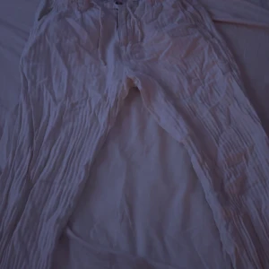 Vita linnebyxor från Lindbergh - Säljer ett par vita linnebyxor från Lindbergh med avslappnad passform och resår i midjan med snörning. Byxorna har en lätt skrynklig struktur och är perfekta för varma dagar. Stilrena och enkla att matcha med olika toppar.