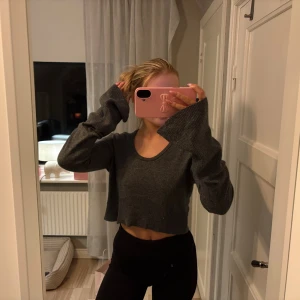 Mörkgrå croppad stickad tröja - Säljer en mörkgrå croppad stickad tröja med lång ärm och rund halsringning. Tröjan har en loose passform och är perfekt för lager-på-lager. Stilren och enkel att matcha med både jeans och kjol.