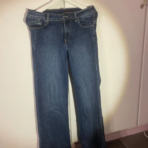 Mörkblå jeans med fin detalj - Ett par mörkblå jeans som är utsvängda i benen. Dem är aldrig använda men har dock ingen prislapp kvar. Skulle säga att dem inte är högmidjade utan något emellan det och låg midjat. Med fin stjärn detalj på ena fickan. Passar lite kortare ben.