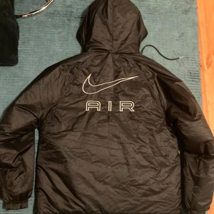  Nike jacka med huva - Svart Nike Air jacka med huva och halv dragkedja. Jackan har broderad Nike-logga och AIR-tryck både fram och bak. Praktisk känguruficka framtill och justerbar dragsko i huvan. Lätt och sportig design i syntetmaterial, perfekt för blåsiga dagar. Riktigt snygg och varm. Perfekt nu för hösten och vintern. In princip helt ny inga fel på den alls.