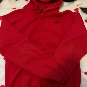 Röd hoodie med tryck från Gildan - Röd hoodie från Gildan med snörning i huvan och svart broderad logga på bröstet. Baksidan har ett stort tryck med konstmotiv och citat av Neil deGrasse Tyson. Tillverkad i en mjuk bomullsblandning, perfekt för dig som gillar unika detaljer och statement-plagg.