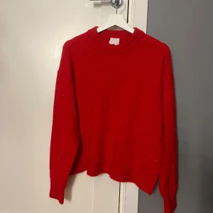 Röd stickad tröja med pärldetaljer H&M - Röd stickad tröja från H&M i storlek S. Tröjan har rund halsringning, långa ärmar och små pärldetaljer utspridda över hela framsidan. 