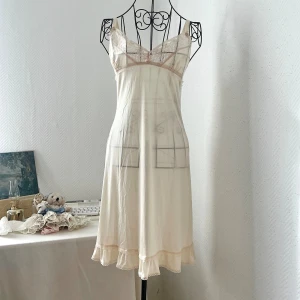 Ljusgul nattlinne med spetdetaljer - Ljusgul/ljus beige nattlinne med spetdetaljer både framtill och nedtill. Delvis genomskinlig. Passar bäst storlek 32-34. Dockan har storlek 34. 