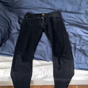 Svarta Lee Jeans - Svarta jeans från Lee, modell Daren Zip Fly. Klassisk femficksdesign med dragkedjegylf och raka ben. Jeansen är tillverkade i bomull och har en stilren look som passar till det mesta. Snygg passform och diskreta detaljer.