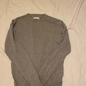Grå stickad tröja  - En enkel och stilren grå stickad tröja.Tröjan har rund halsringning och långa ärmar, perfekt för lager-på-lager under kyliga dagar. Mjuk och bekväm, passar till det mesta i garderoben.