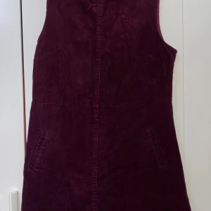 Vinröd manchesterklänning från Oasis - Snygg vinröd kortklänning från Oasis i mjuk manchester. Klänningen är ärmlös med rund halsringning och har praktiska fickor framtill. Stängs med dragkedja i ryggen. Perfekt för dig som gillar retrovibbar och vill sticka ut med färg. En kort klänning som är jättefin och som passar för hösten! Längden är 84 cm och bredden (från ena axeln till det andra) är 35 cm. Meddela gärna för mer info! 💕