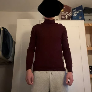 Vinröd polotröja från J.Lindeberg - Vinröd polotröja från J.Lindeberg i slim passform. Tröjan är stickad och har långa ärmar samt en klassisk polokrage. Perfekt för dig som gillar stilrena och tidlösa plagg med en modern touch.