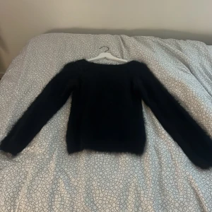 Svart fluffig stickad tröja - Mysig svart stickad tröja med fluffig yta och rund hals. Tröjan har långärmade ärmar och en normal passform som sitter snyggt på kroppen. Perfekt för dig som gillar en enkel men ändå cool look med lite extra textur.