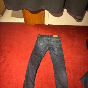 Mörkblå slim jeans från tiger of sweden  - Säljer ett par mörkblå slim jeans från tiger of sweden med klassiska fem fickor och snygga slitningar. Jeansen har låg midja och smal passform som sitter tight hela vägen ner. Perfekta för dig som gillar en modern och stilren look.
