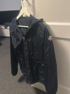Blå vindjacka från Moncler - Snygg blå vindjacka från Moncler. Jackan har långa ärmar och en diskret logga på ärmen. Perfekt för blåsiga dagar och en stilren look. Säljer den då den nu är för liten. Hör av er vid minsta fråga samt för att få fler bilder!