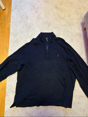 Marinblå half zip tröja Polo Ralph Lauren - Säljer en marinblå långärmad tröja från Polo Ralph Lauren i storlek XXL. Tröjan har half zip-dragkedja, hög krage och den klassiska röda broderade loggan på bröstet. Perfekt för dig som gillar en clean och stilren look. Använd rätt många gånger men lyckats hålla den i bra skick.