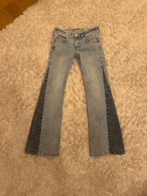 Lågmidjade Bootcut jeans från Divided H&M, stl 34 - Säljer ett par ljusblå bootcut jeans från Divided H&M i storlek 34. Jeansen har coola mörkblå paneler längs utsidan av benen och slitna detaljer längst ner vid bensluten.                                              !PRIS KAN DISKUTERAS!