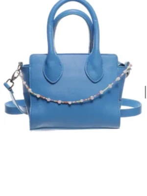 Blå axelväska med pärldetalj - Snygg blå axelväska i skinn med två handtag och avtagbar axelrem. Väskan har en söt pärlrem framtill som ger en lekfull touch. Perfekt storlek för det viktigaste och enkel att matcha med olika outfits.