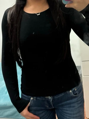 Svart långärmad topp i bomull - En enkel och stilren svart långärmad topp i mjuk bomull. Modellen är figurnära med rund halsringning och passar perfekt till jeans eller kjol. Toppen är helt utan mönster och har en klassisk look som funkar till det mesta.
