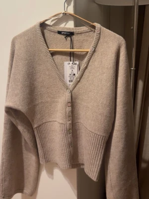 Trendig stickad kofta perfekt basplagg helt ny! - Superfin stickad kofta i en tidlös beige/ljusbrun nyans – ett riktigt capsule wardrobe-plagg 🤍 Perfekt både till vardag och mer uppklädda outfits. Funkar lika bra till jeans som över klänning eller kjol. Detaljer: 	•	Mjuk och skön stickning 	•	Smickrande V-ringning 	•	Knäppning framtill 	•	Ribbad midja (väldigt trendigt just nu!) 	•	Lätt att styla året runt  Storlek: S Skick: Ny / mycket fint skick (med lapp kvar) Märke: Gina Tricot Snabb frakt!!