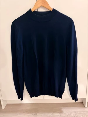 Mörkblå stickad tröja - En enkel och stilren mörkblå stickad tröja med rund hals och långa ärmar. Perfekt att matcha med jeans eller kjol för en clean look. Tröjan har en klassisk passform och mjukt material som känns skönt mot huden. 100% ull !! 