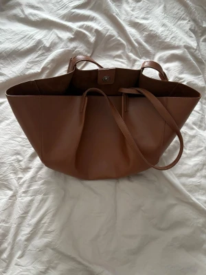 Brun väska  - Brun väska från Nakd. Slutsåld, aldrig använd. 549 nypris.  Höjd: 24.5 cm i storlek One Size Längd: 42 cm i storlek One Size Vidd: 14 cm i storlek One Size