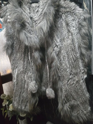 Äkta grå fluffig pälsväst (Angelique.L med huva) - Säljer en supermysig (nästan oanvänd)  grå pälsväst med stor huva och fluffiga kanter. Västen har snören med bollar framtill och en riktigt mjuk känsla. Perfekt för dig som vill ha något extra till din outfit och gillar att sticka ut lite.  Material enligt etikett: 30% marmot, 70% lapin (kanin).