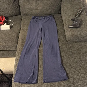 Mörkblå vida byxor Gina Tricot XXS - Mörkblå byxor från Gina Tricot i supermjuk polyester med breda ben och hög midja. Byxorna har två dekorativa öljetter fram i midjan och en riktigt chill, loose passform. Perfekta för dig som gillar bekväma och trendiga plagg.